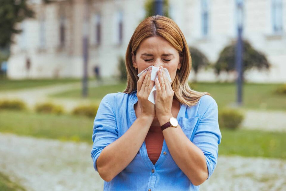 A woman in a park blowing her nose, possibly dealing with fungal sinusitis in Burbank, CA.