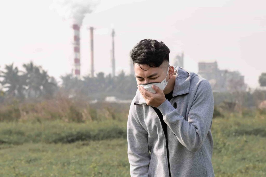 A masked man stands in a field, factory in the background, symbolizing rhinologic diseases in Burbank, CA.