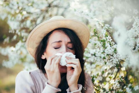 A woman dealing with spring allergies blows her nose in front of a tree in Burbank, CA.