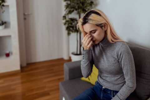 A woman seated on a couch, hand on her face, expressing thoughtfulness in a cozy space in Burbank, CA.