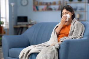 A woman seated on a couch, tissue in hand, indicating sinusitis symptoms in Burbank, CA